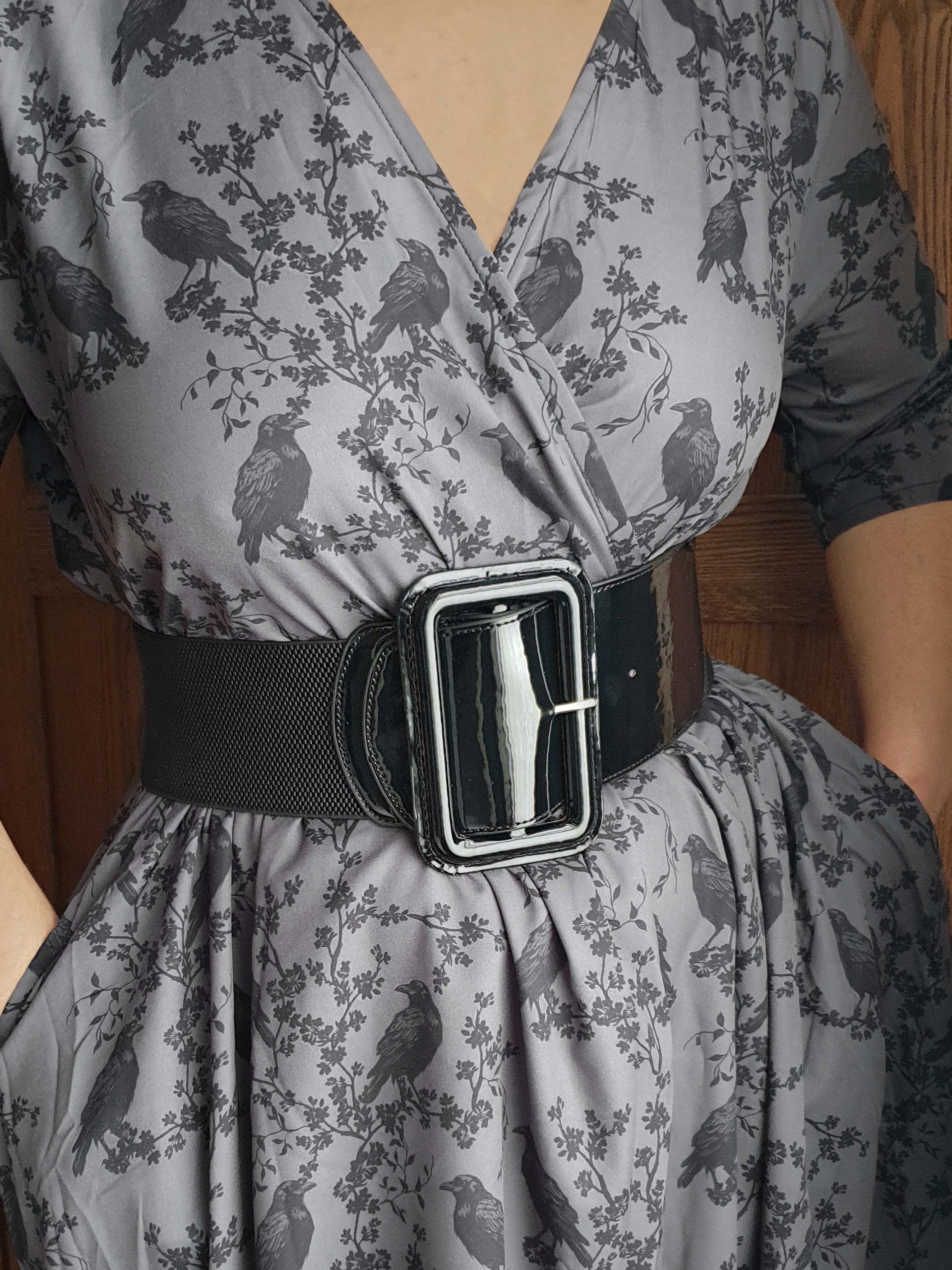 Gray dress with black ravens &amp; blossoms pattern and black belt worn by a person against a wooden door background