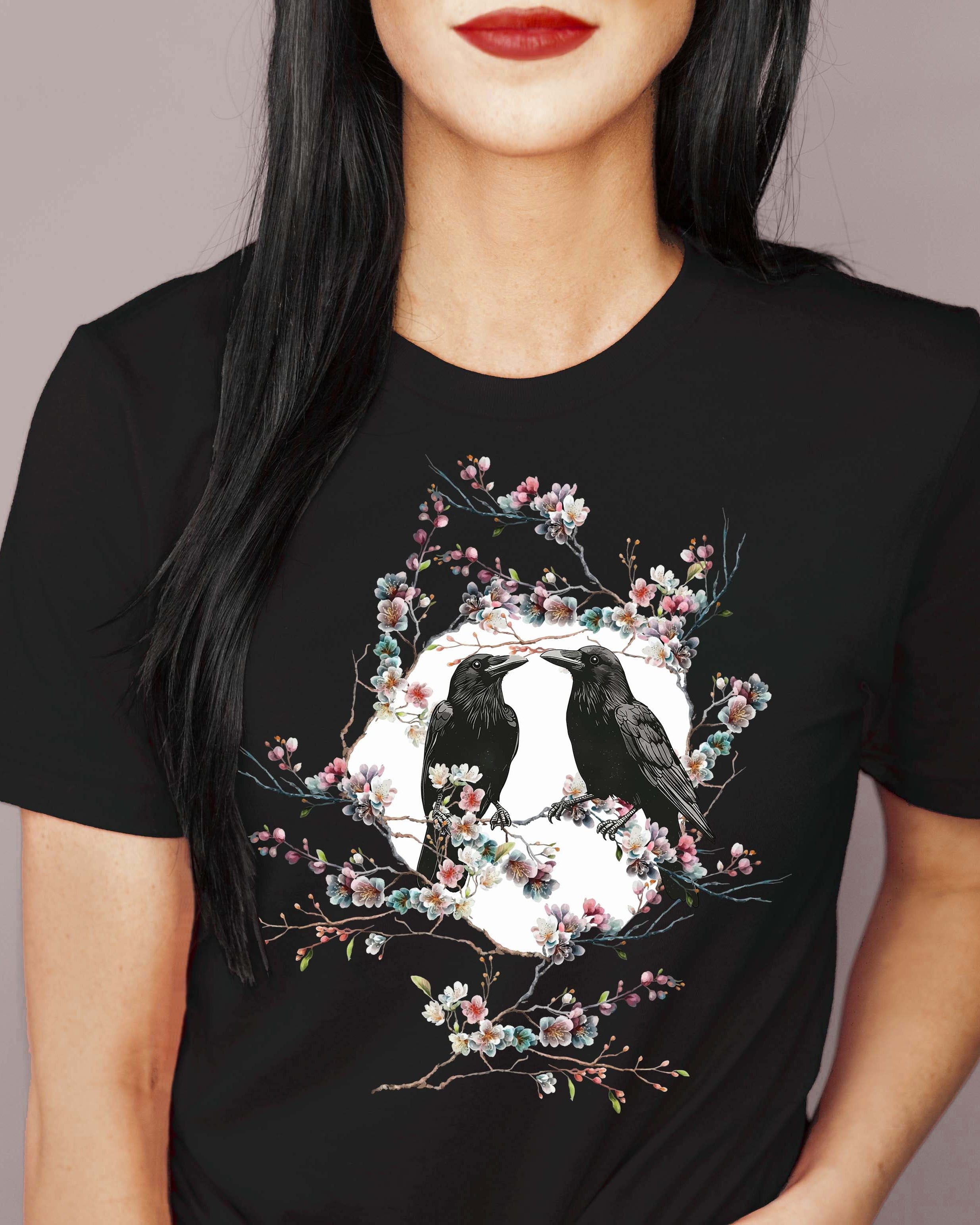 Black t-shirt with a design of two crows in a floral circle worn by a person.